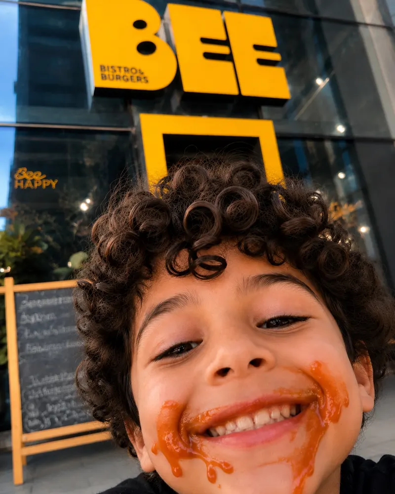 Smiling curly-haired boy with sauce on his face in front of the BEE storefront
